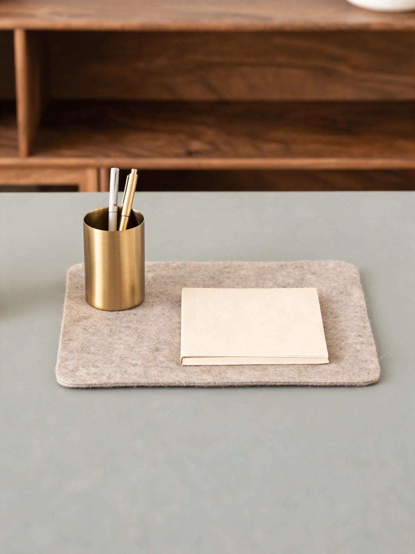 Walnut desk shelf with a felt mat and a brass pen cup on a matte grey desk